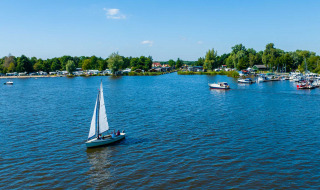 Velero en un lago cerca de Sumar, Frisia, Países Bajos, rodeado de árboles y barcos en el fondo
