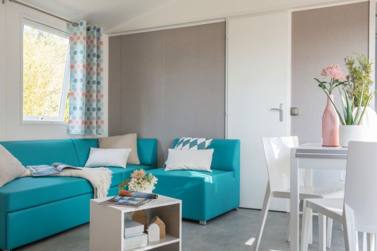 Luminoso salón moderno en la Lodge XL de Vakantiepark Bergumermeer, Países Bajos, con sofá azul y mesa blanca.