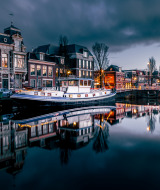 Canal pintoresco al atardecer con barco casa, edificios históricos y luces reflejadas en el agua tranquila.