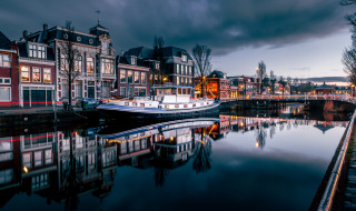 Canal pintoresco al atardecer con barco casa, edificios históricos y luces reflejadas en el agua tranquila.