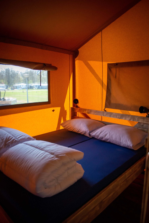 Vista interior de una tienda safari con cama matrimonial y almohadas en Vakantiepark Bergumermeer, Países Bajos.