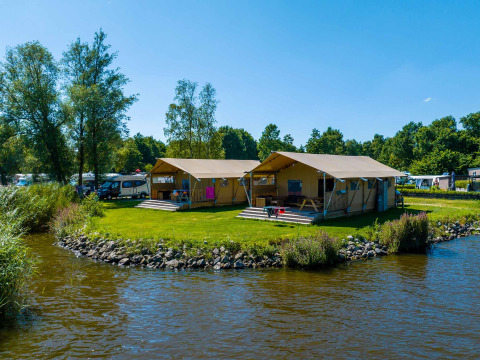 Safari tents by the water at Vakantiepark Bergumermeer in the Netherlands, surrounded by lush greenery.