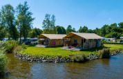 Safari-telte ved søen i Vakantiepark Bergumermeer, Holland, omgivet af grønne træer og vand.