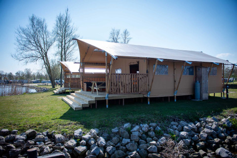 Safari tent lodge beside the lake at Vakantiepark Bergumermeer, Netherlands, featuring a wooden veranda.