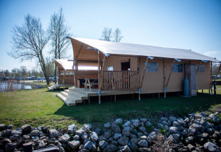 Safari tent lodge beside the lake at Vakantiepark Bergumermeer, Netherlands, featuring a wooden veranda.