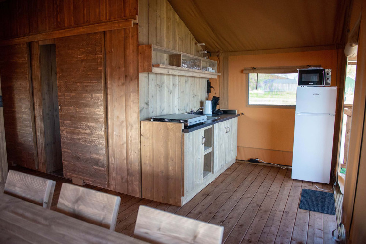 Innenansicht eines Safarizelts im Vakantiepark Bergumermeer, Niederlande, mit Holzmöbeln und Küche.