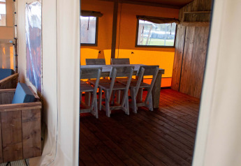 Entrada a la tienda Safari en Vakantiepark Bergumermeer, Países Bajos, con mesa y sillas de madera.