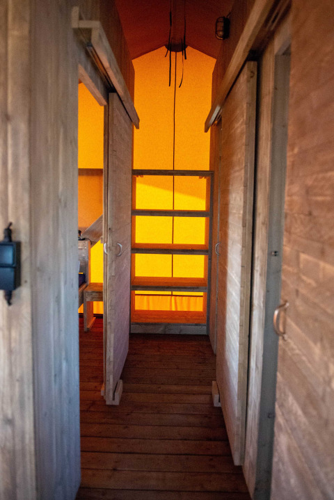 Vista interior de una tienda safari con paredes de madera y luz naranja en Bergumermeer, Países Bajos.