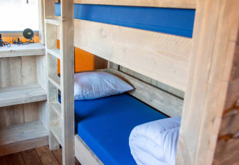 Køjeseng i en safaritelt-lodge på Vakantiepark Bergumermeer, Holland, med træinteriør og blå madrasser.