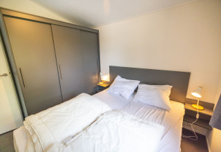 Dormitorio con cama doble, cabecero gris y armarios en Waterlodge tipo 2, Vakantiepark Bergumermeer, Países Bajos.