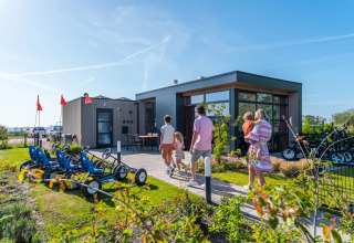 Familia llega a una moderna cabaña glamping en un parque de vacaciones con karts y bicicletas afuera.