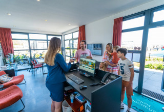 Gezin meldt zich aan bij de receptie van een glamping-vakantiepark, hartelijk ontvangen door receptioniste.