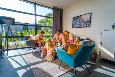 Familia disfrutando de alojamiento moderno y luminoso en un parque de glamping con grandes ventanales y sofás cómodos.