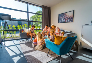 Familia disfrutando de alojamiento moderno y luminoso en un parque de glamping con grandes ventanales y sofás cómodos.