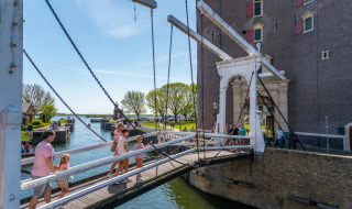 Familien überqueren eine Zugbrücke bei einem historischen Gebäude in einem malerischen Ferienpark.