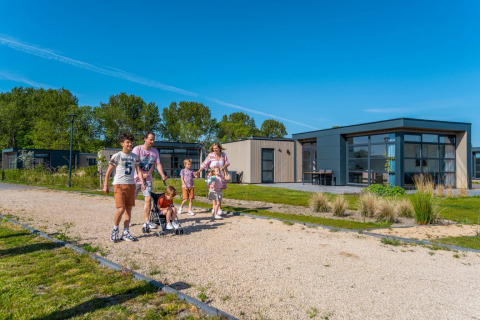 Familie nyder en gåtur foran moderne glamping-hytter i en feriepark på en solrig dag.
