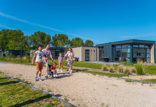 Family enjoying a walk in front of modern glamping lodges at a holiday park on a sunny day.