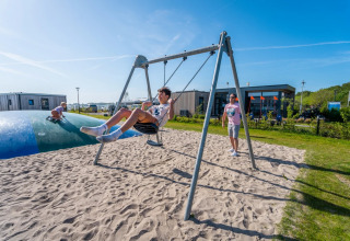 Children play on a swing and jumping pillow at a holiday park with glamping lodges on a sunny day.