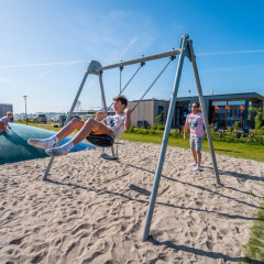Kinder spielen auf einer Schaukel und Hüpfkissen in einem Ferienpark mit Glamping-Unterkünften.