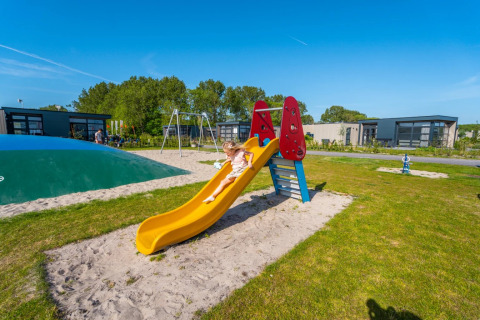 Child sliding down a playground slide at a holiday glamping park with modern cabins in the background.