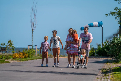 Een gezin loopt door een vakantiepark met glamping, ouders en kinderen genieten van een zonnige dag.