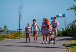 Een gezin wandelt door een glampingvakantiepark, ouders en kinderen genieten van het zonnige buitenleven.