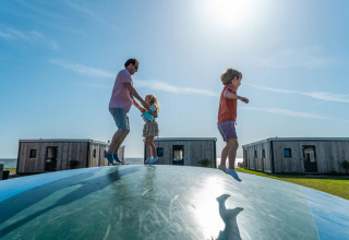 Famiglia che si diverte su un grande cuscino ad aria davanti a lodge glamping in un soleggiato villaggio vacanze.