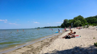 Menschen entspannen sich am Sandstrand eines Ferienparks mit Glamping-Angeboten am Wasser.