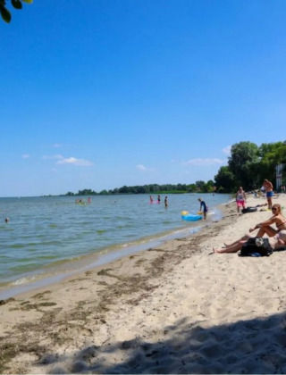 Personas descansando y nadando en una playa junto a un parque vacacional con opciones de glamping.