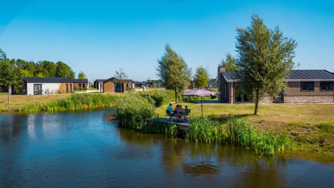 Foto van een vakantiepark met glamping, vijver, moderne chalets en gasten die genieten aan het water.