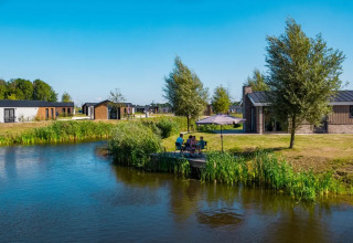 Foto van een vakantiepark met glamping, vijver, moderne chalets en gasten die genieten aan het water.