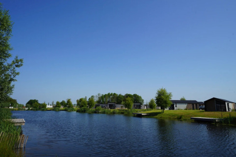 Parque vacacional con alojamientos glamping junto a un lago, rodeado de árboles y cielo azul claro.