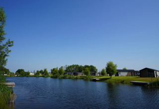 Vakantiepark met luxe glampinghutten aan een meer, groene natuur en een heldere blauwe hemel.