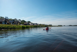 Village vacances avec hébergements glamping au bord du lac, couple en kayak rouge sur l’eau calme.