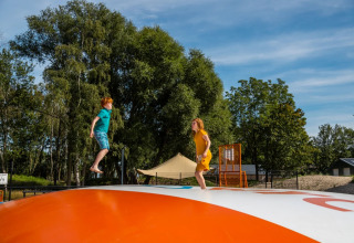 Twee kinderen spelen op een springkussen in een vakantiepark met glampingaccommodatie.