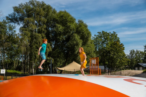 Zwei Kinder springen auf einem aufblasbaren Kissen in einem Ferienpark mit Glamping-Unterkünften.