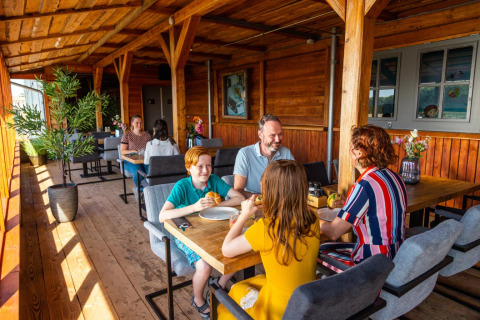 Famiglia che si gode un pasto su una terrazza di legno coperta in un glamping all'interno di un villaggio vacanze.