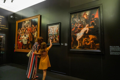 Une femme et une fillette regardent des peintures classiques dans une galerie de musée aux murs sombres.