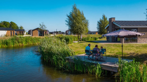 Familie nyder udsigten ved en sø, omgivet af moderne glamping-hytter i en feriepark på en solskinsdag.