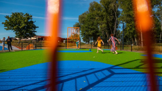 Niños y adultos juegan en un colorido parque infantil de césped artificial en un parque de vacaciones, visto a través de una valla.