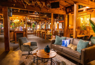 Knusse lounge in een vakantiepark met houten interieur, comfortabele zetels en tafeltjes om te ontspannen.