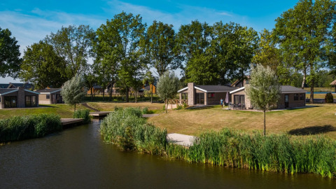 Photo of glamping accommodations by a lake at a holiday park, featuring modern cabins and green lawns.