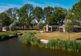 Foto van glampingverblijven aan een vijver in een vakantiepark met moderne chalets en groene grasvelden.