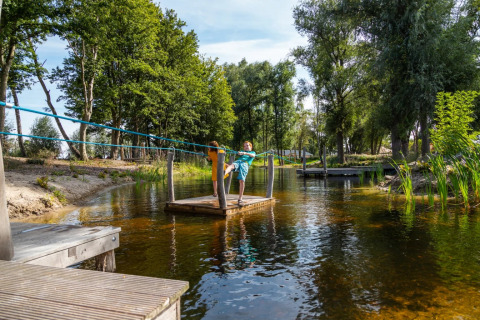 Enfant tirant un radeau sur un étang dans un parc de vacances avec hébergements glamping en pleine nature.