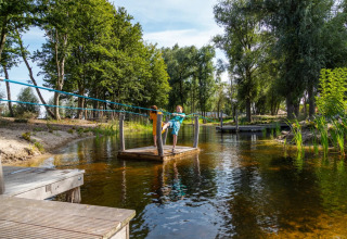 Bambino trascina una zattera su uno stagno in un parco vacanze dotato di sistemazioni glamping immerse nel verde.