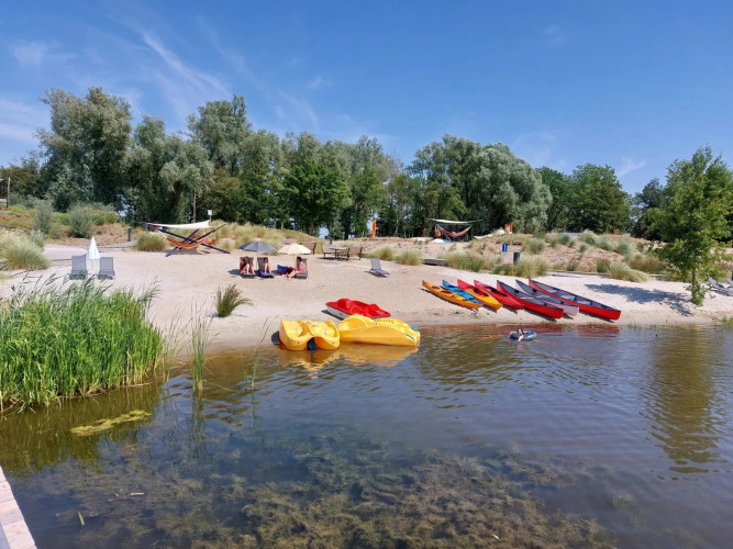 Strand met kajaks, waterfietsen, hangmatten en gasten bij bomen in een glampingvakantiepark.