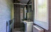 Moderne badkamer in Forest Cottage op Recreatiepark de Paalberg, Nederland, met douche en witte jaloezieën.