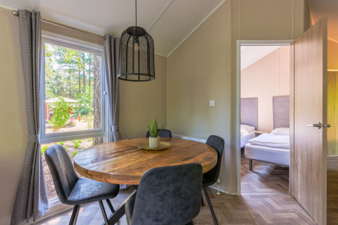 Dining area with round wooden table, modern chairs and forest view at Forest Cottage in Recreatiepark de Paalberg.