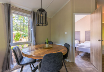 Salle à manger avec table ronde en bois, chaises modernes et vue sur la forêt à Forest Cottage, Recreatiepark de Paalberg.