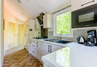 Moderne køkkenindretning med store vinduer, kaffemaskine og mikrobølgeovn i Forest Cottage, De Paalberg.